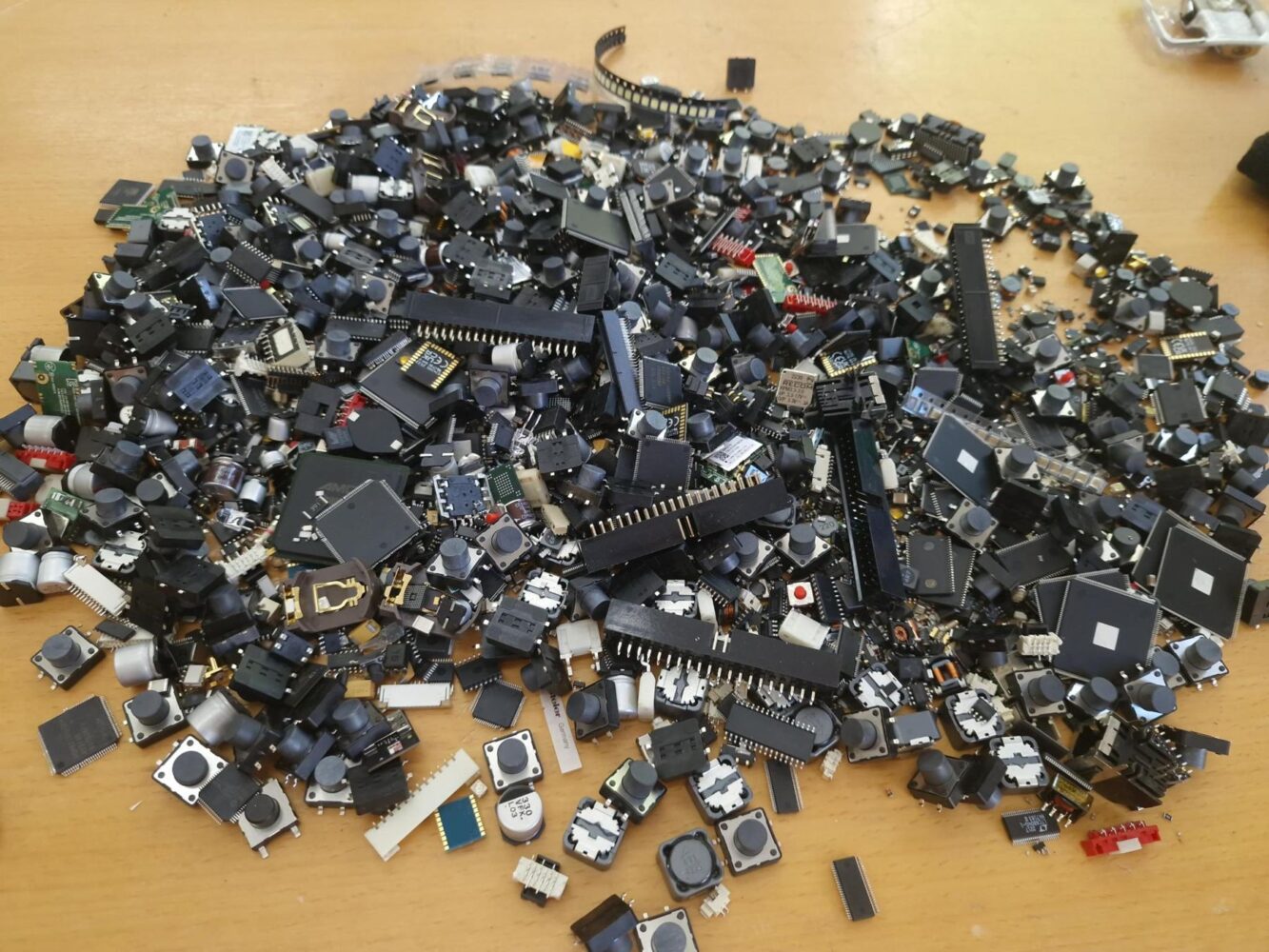 Aus Altgeräten zurückgewonnene elektronische Bauteile – Taster, Chips, Steckverbinder und Spulen – auf einem Werktisch